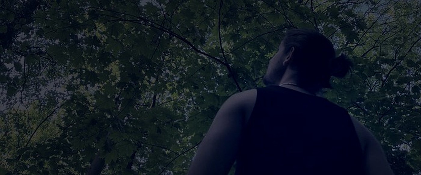 Alessandro standing beneath forest canopy, seen from behind
