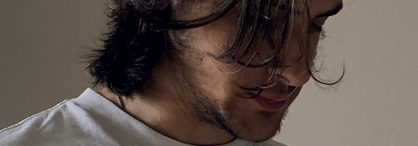 Alessandro with his head bowed, hair falling over his face, alone in a quiet room